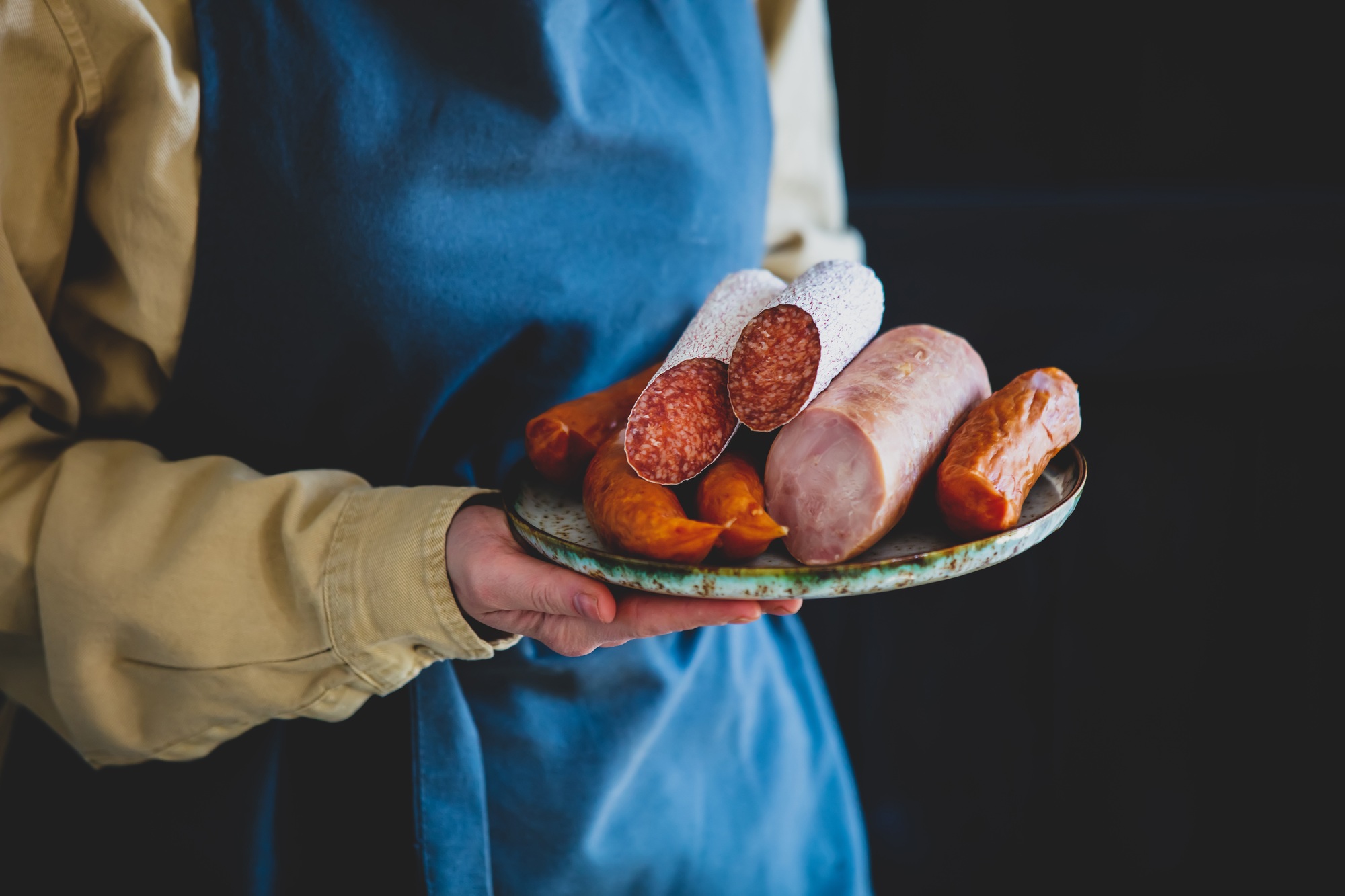 Woman in apron holds plate with salami and other sausages